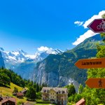 Road sign with arrows for hiking and biking tourist trails pointing fork in the road from village Wengen to Lauterbrunnen, Bernese Oberland, Switzerland. The Jungfrau is visible in the background